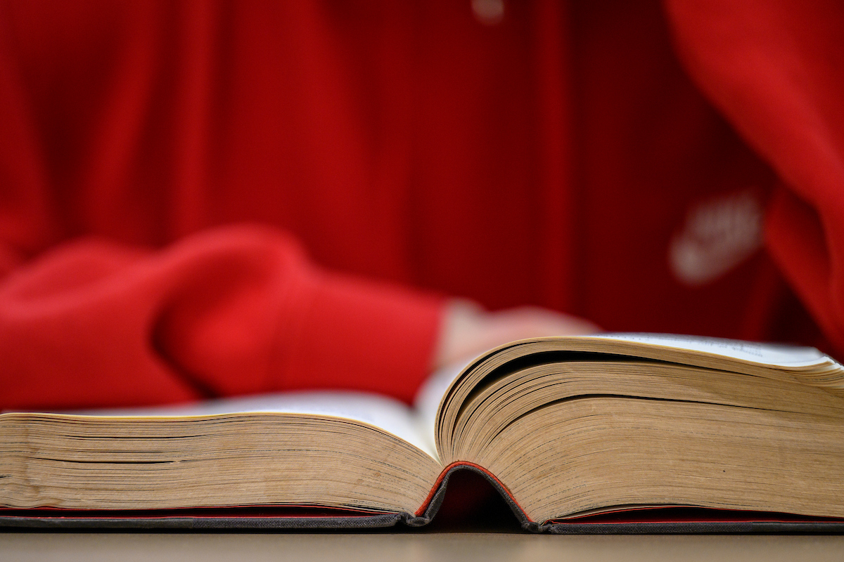 A student in a red sweater reads an old, well-worn book.