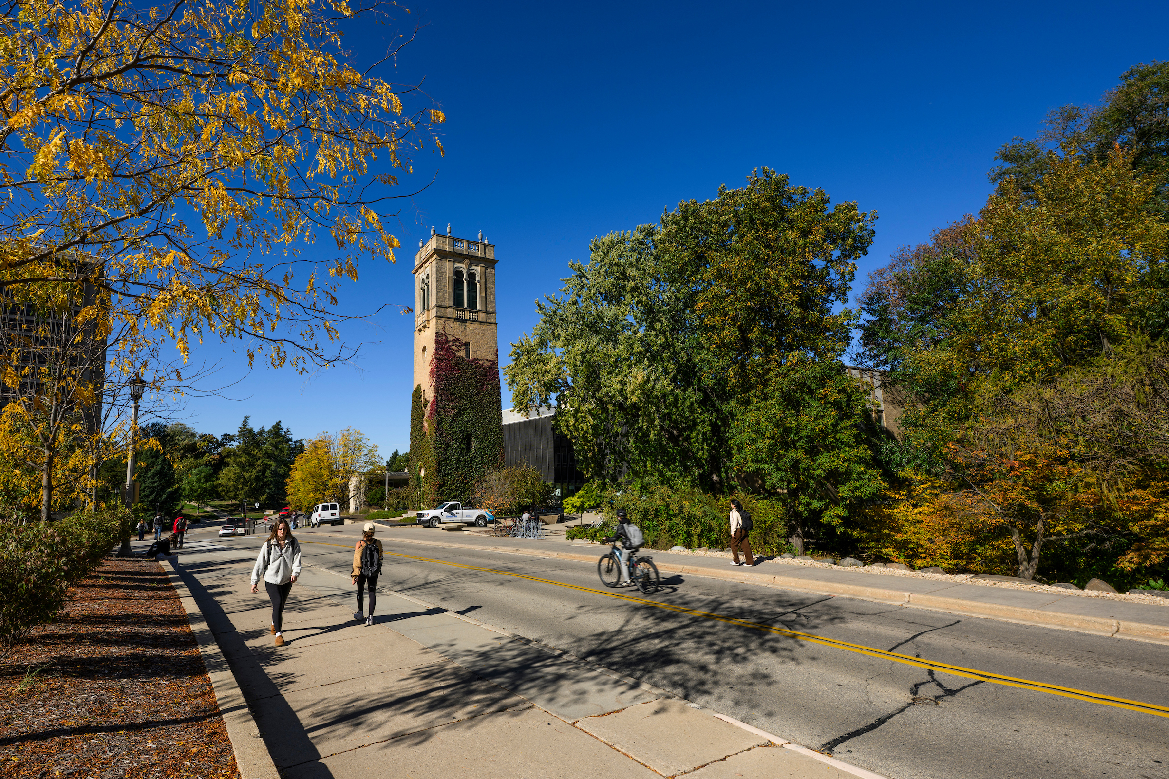 Students, bikers, and campus community members pass Carillon Tower on Observatory Hill as the trees begin to show fall color during a sunny autumn day at the University of Wisconsin–Madison on Oct. 20, 2025. (Photo by Taylor Wolfram / UW–Madison)